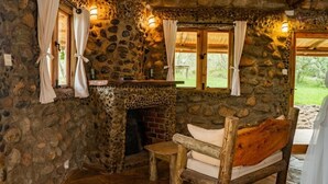 Una habitación rústica con paredes de piedra, chimenea, muebles de madera y ventanas con cortinas.