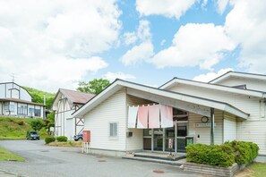 A two-story building with a sloped roof, a covered entrance, and a small garden area in front.