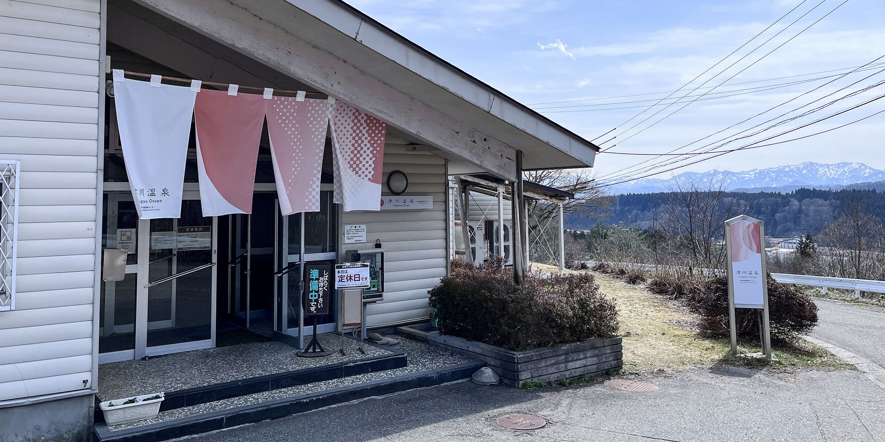 A building with a covered entrance, a signboard, and a view of mountains in the background.