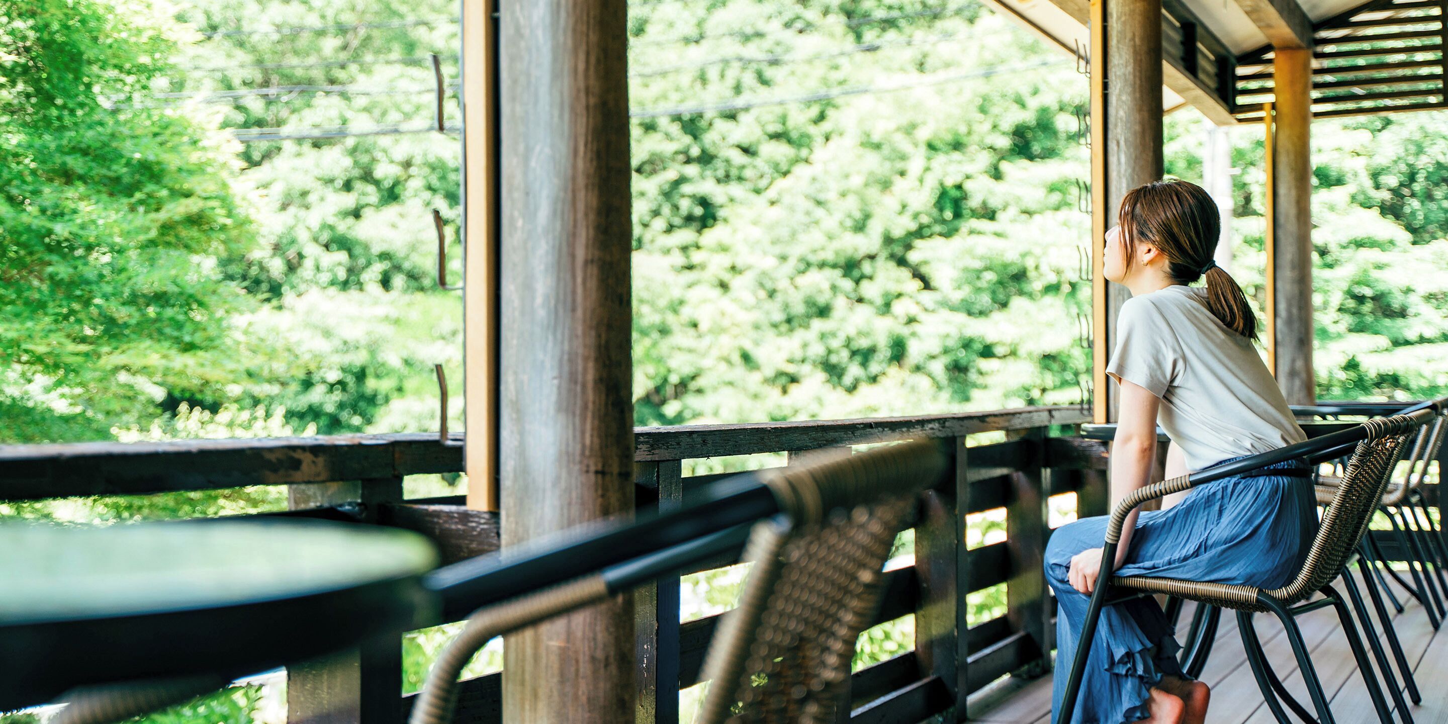 A person sitting on a wicker chair on a wooden deck with a view of greenery.