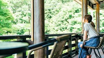 A person sitting on a wicker chair on a wooden deck with a view of greenery.