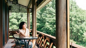 A person sitting at a table on a wooden deck with a view of dense green trees. - Kiyokawa High-land Recreation Center (Aga)