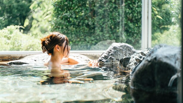 A person relaxing in a hot spring with a view of lush greenery through a window. - Kiyokawa High-land Recreation Center (Aga)
