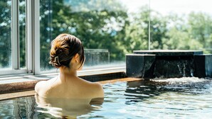 A person in a hot tub with a view of trees and a stone structure. - Kiyokawa High-land Recreation Center (Aga)