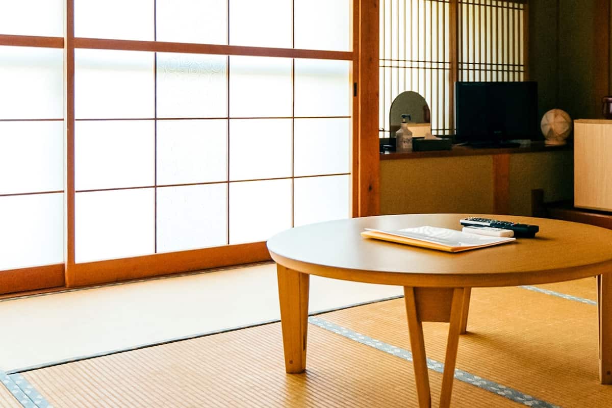 Een kamer met tatami matten en een tatami vloer, een ronde houten tafel met een boek en afstandsbediening, een televisie en een kast.