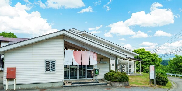 A white building with a sloped roof, a small porch, and a signboard.