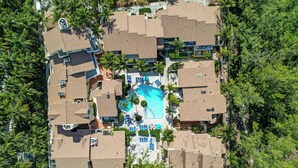 Ein Luftbild eines Resorts mit mehreren bungalowartigen Gebäuden, einem zentralen Swimmingpool und umliegenden Palmen.
