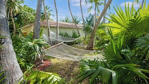 Eine Hängematte in einem üppigen Garten mit Palmen und einem Gebäude im Hintergrund.