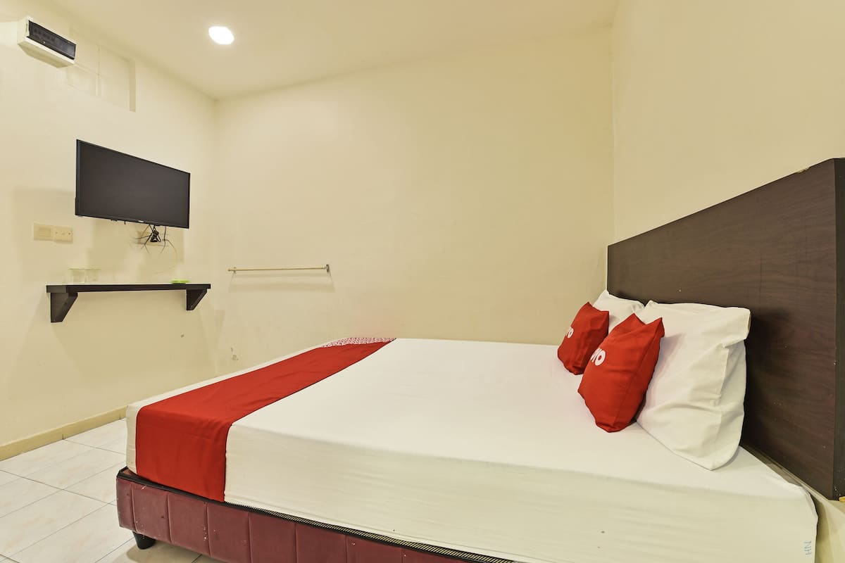 A neatly made bed with a red and white bedspread, two red pillows, and a dark headboard.