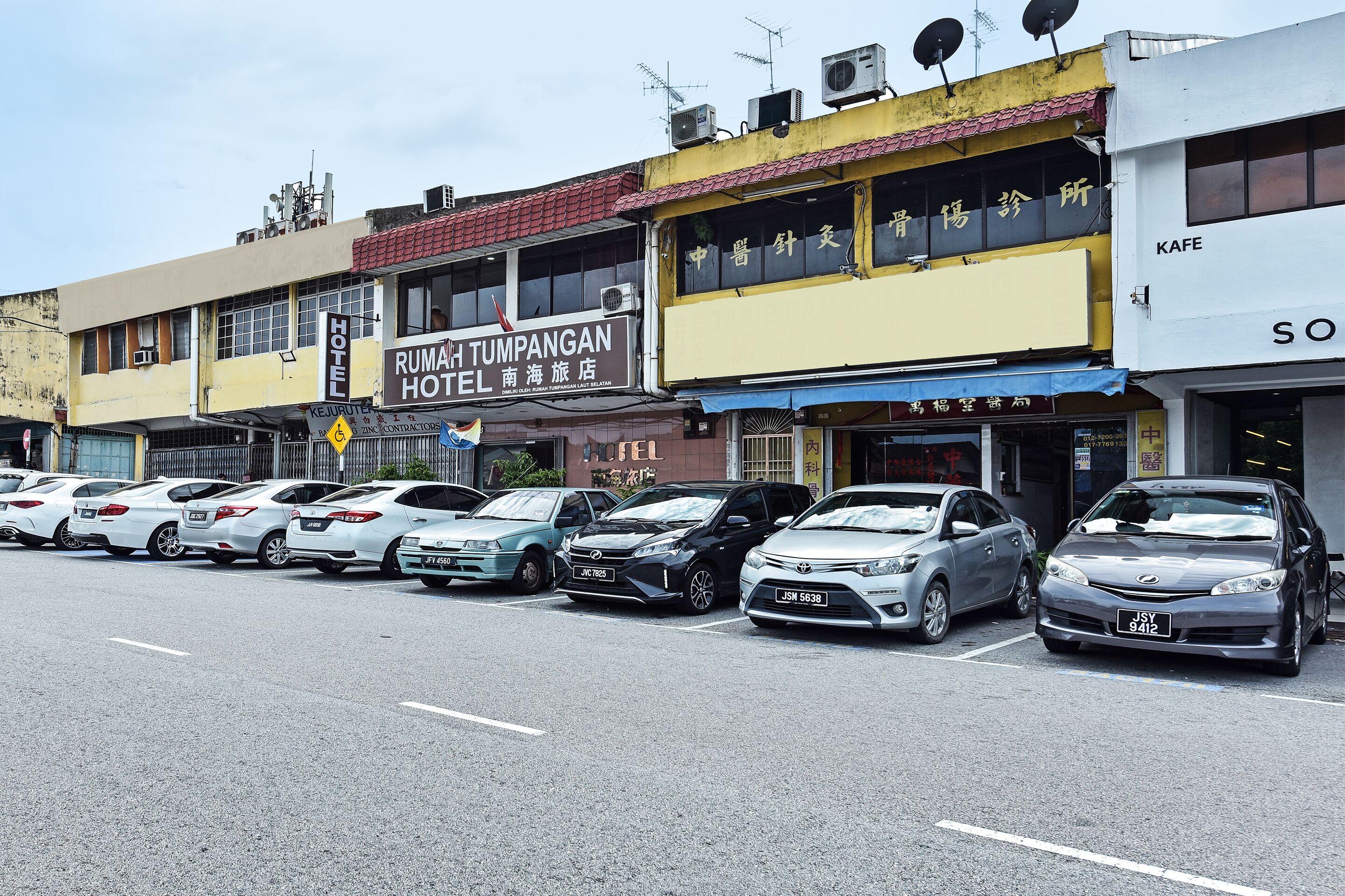 A row of parked cars in front of a hotel with a sign for 'Rumah Tumpangan Hotel'.