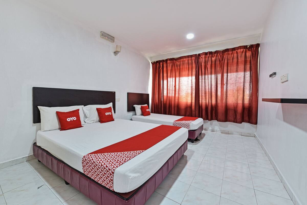 A hotel room with two beds, red and white bedding, a red curtain, white walls, and a tiled floor.