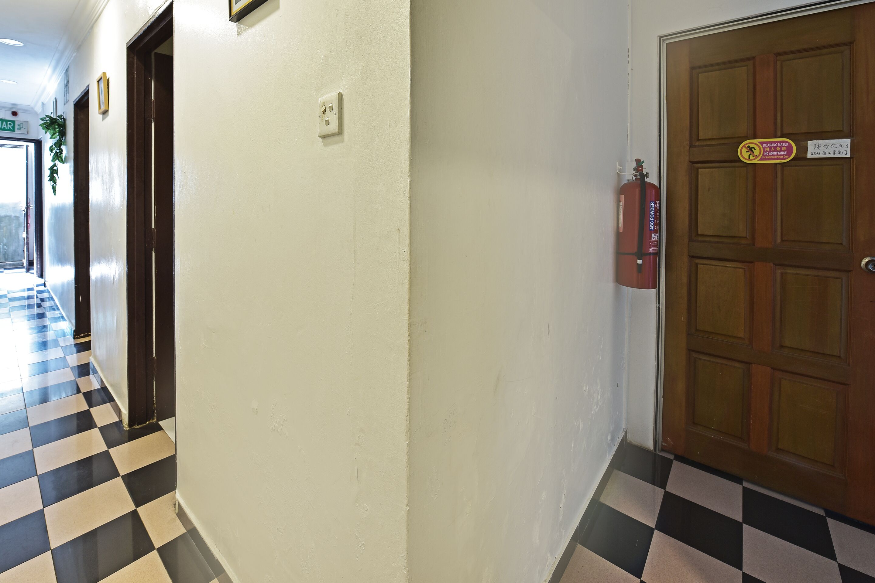 Un corridoio d'albergo con pavimento a scacchi, una porta in legno con estintore e un cartello che indica una zona fumatori.