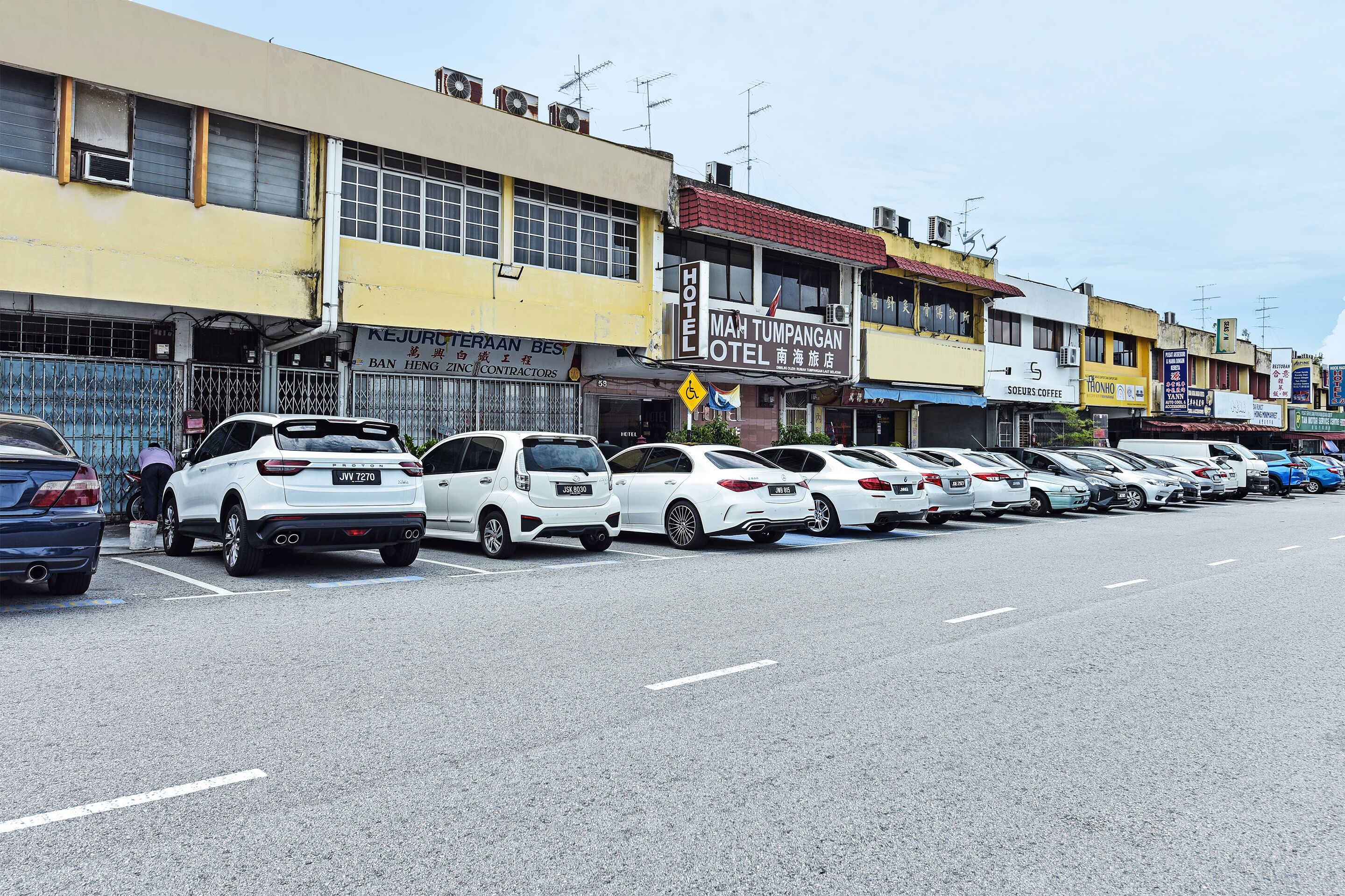 A row of white cars parked along a street with buildings featuring signs for a hotel and other businesses.