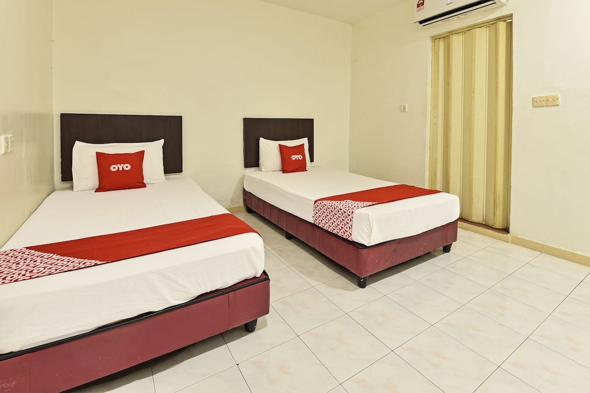 Two single beds with white and red bedding, a dark headboard, and a red pillow with "OYO" text.