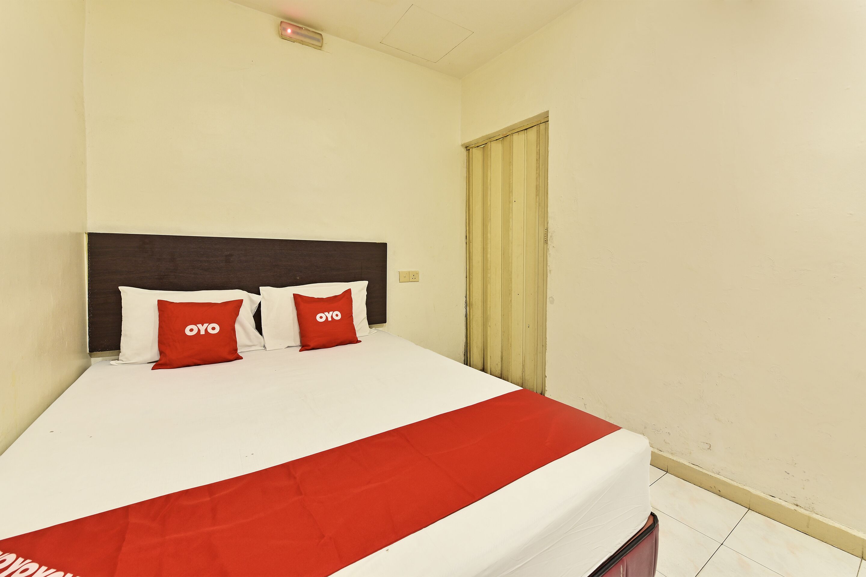 Une chambre d’hôtel avec un lit, deux oreillers rouges portant la marque « OYO », une couvre-lit rouge et une tête de lit en bois.
