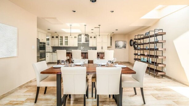 A modern dining room with a wooden table set for six, white chairs, and a kitchen in the background. - McCormick Ranch Oasis (Scottsdale)
