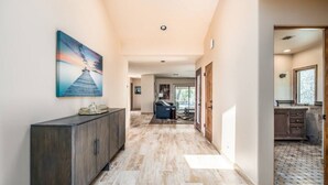 A spacious hallway with a wooden cabinet, a painting, and a view into a living area with a sofa and a dining table. - McCormick Ranch Oasis (Scottsdale)