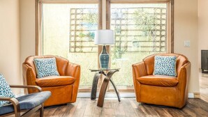 A room with two leather armchairs, a small table with a lamp, and large windows with a view of greenery. - McCormick Ranch Oasis (Scottsdale)