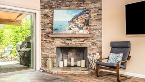 A living room with a stone fireplace, a mounted TV, and a comfortable chair. - McCormick Ranch Oasis (Scottsdale)