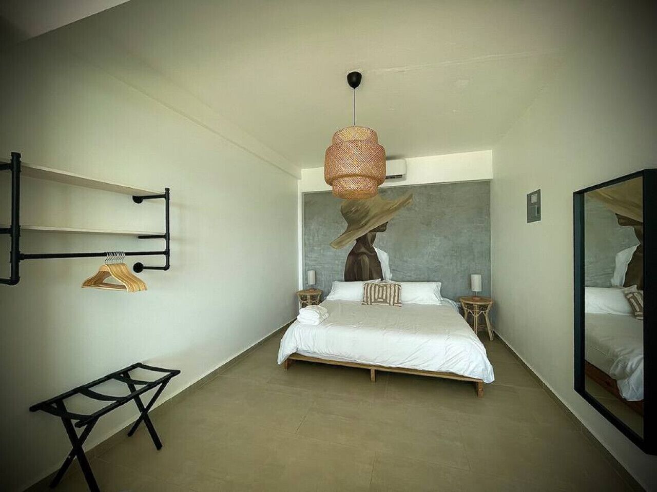 A modern bedroom with a large bed, a hanging light fixture, a mirror, and a small table.