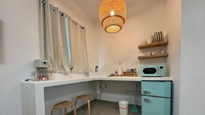 Eine kleine Küche mit weißer Arbeitsplatte, zwei Holz-Barhocker, einem türkisblauen Kühlschrank, einer Mikrowelle und einer Pendelleuchte.
