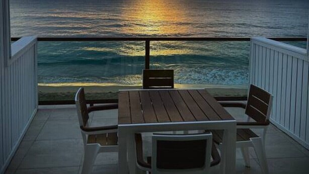 Ein Balkon mit Holztisch und -stühlen mit Blick auf den Ozean bei Sonnenuntergang.