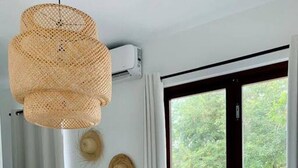 A room with a white table and chairs, a woven pendant light, a window with curtains, and a wall-mounted air conditioning unit. - Corcega Beachfront Suite with Balcony in Rincon (Aguada)