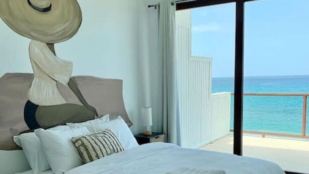 A bedroom with a large bed, a view of the sea, and a balcony. - Corcega Beachfront Suite with Balcony in Rincon (Aguada)