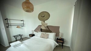 A neatly made bed with white linens, a bedside table with a lamp, and a wall-mounted towel rack. - Corcega Beachfront Suite with Balcony in Rincon (Aguada)