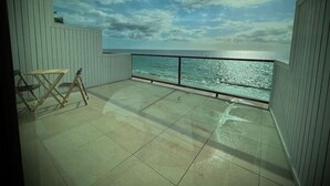 Un balcón con vista al mar, una mesa de madera y una silla.