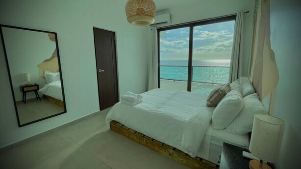 Un dormitorio con una cama grande, un espejo, una ventana con vista al mar y una lámpara colgante.