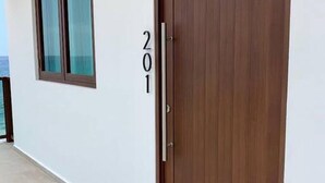 Um corredor com uma porta de madeira marcada com o número 201 e uma janela com vista para o mar.