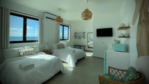 Quarto de hotel com duas camas, televisão, pequena cozinha e vista para o mar.
