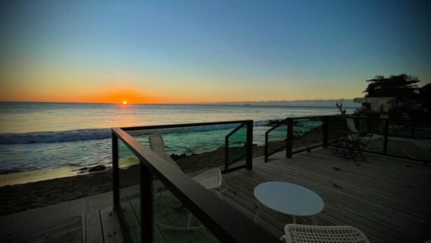 A wooden deck with a table and chairs overlooking the ocean at sunset. - Corner Beachfront Family Suite (Rincon)