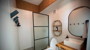 A modern bathroom with a white toilet, a wooden vanity with a sink, and a large mirror. - Corner Beachfront Family Suite (Rincon)
