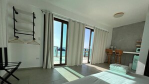 A hotel room with a bed, a desk, a chair, a balcony with a view, and a kitchenette. - Corner Beachfront Family Suite (Rincon)