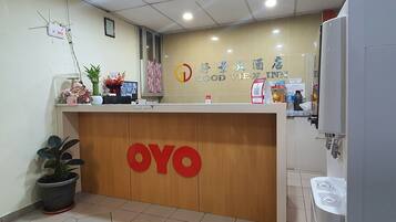 Uma mesa de recepção com bancada de madeira, uma planta em vaso e uma placa com a inscrição "OYO".