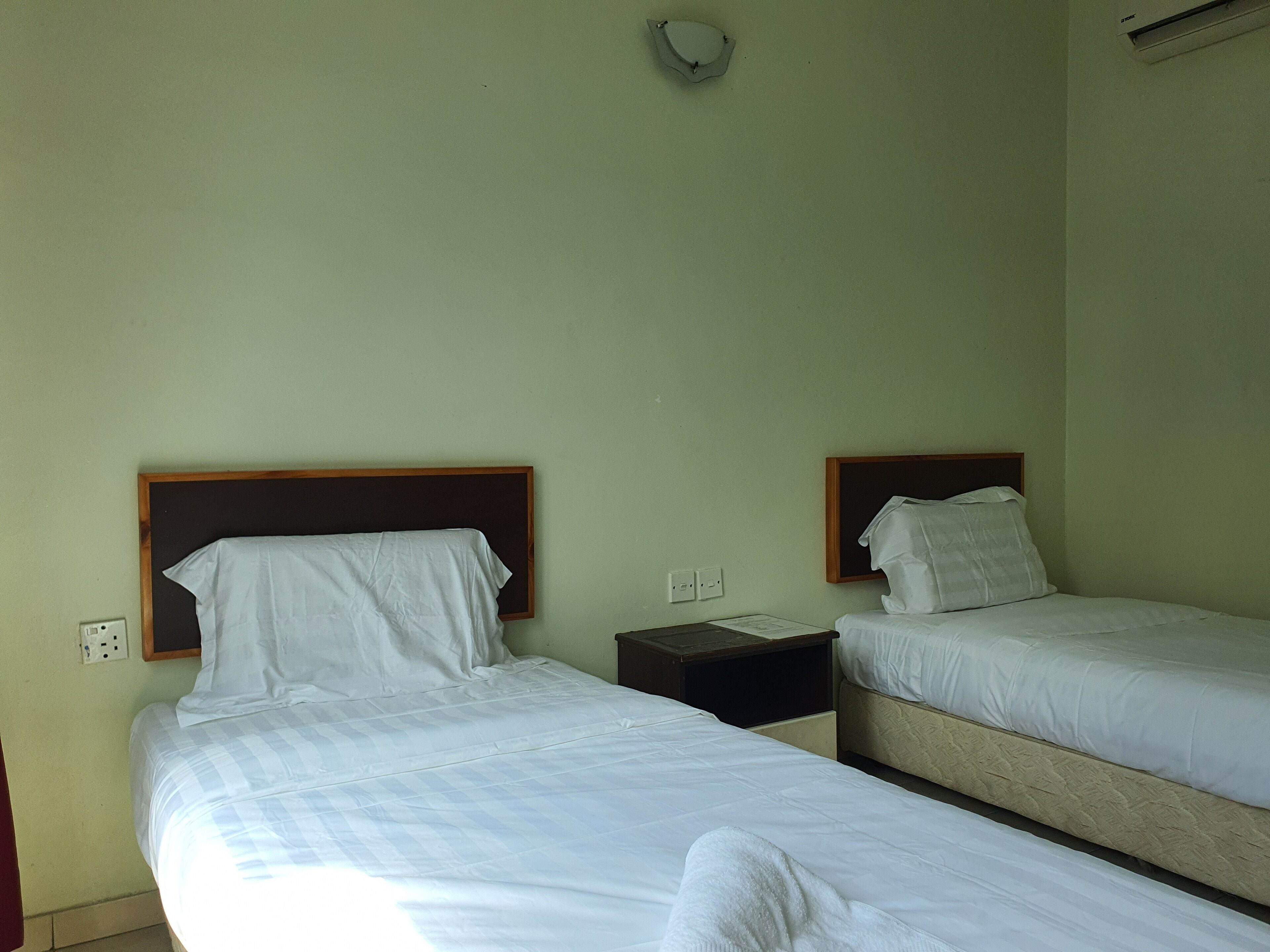 Una habitación con dos camas individuales, cada una con cabecera de madera, ropa de cama blanca y una mesita de noche con lámpara.