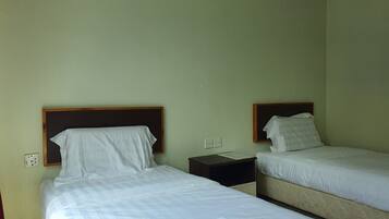 A room with two single beds, each with a wooden headboard, white bedding, and a small bedside table with a lamp.