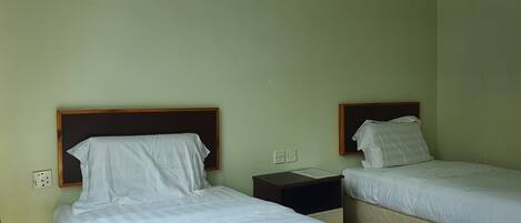 Una habitación con dos camas individuales, cada una con cabecera de madera, ropa de cama blanca y una mesita de noche con lámpara.