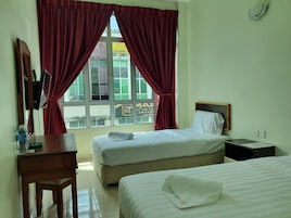 Quarto de hotel com duas camas, uma mesa de trabalho, uma televisão e uma janela com cortinas vermelhas.