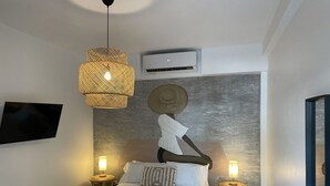 A modern bedroom with a large bed, two bedside tables with lamps, a television on the wall, and an air conditioning unit.