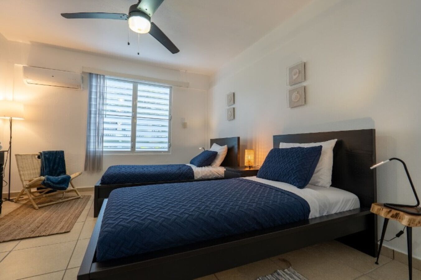 A bedroom with two beds, a ceiling fan, a window with blinds, and a floor lamp.