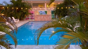 A swimming pool with a view of a building, surrounded by palm trees and string lights.