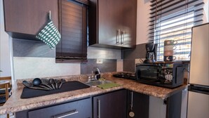 Une cuisine de taille réduite avec des meubles de couleur bois foncé, un plan de travail en granit, un évier, une cuisinière, un four à micro-ondes et une machine à café.