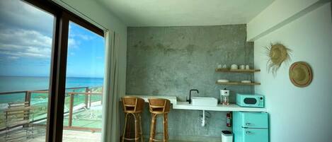 A compact kitchen with a view of the ocean, a small fridge, and two bar stools.