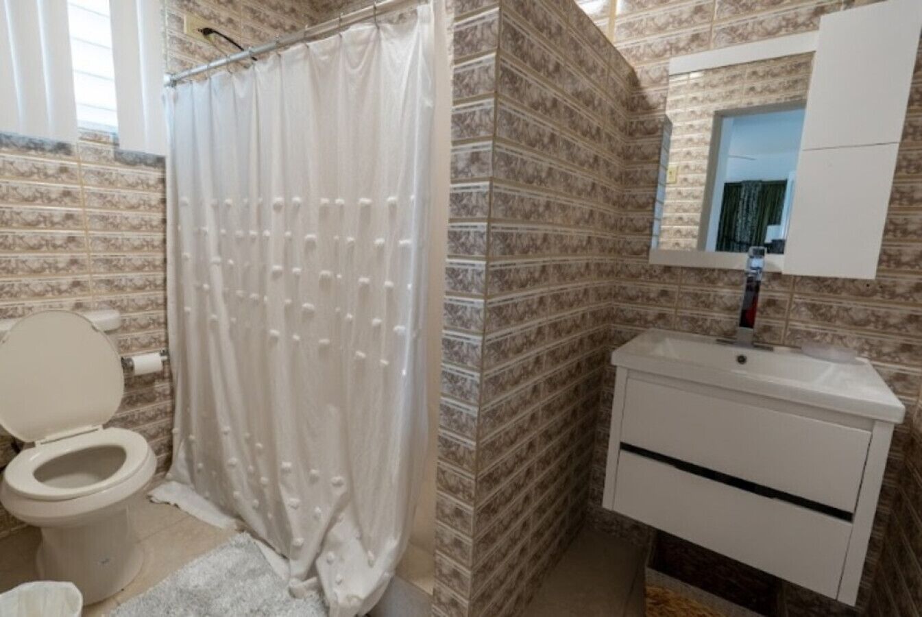 Un bany amb cortina de dutxa, vàter i un lavabo amb un mirall a sobre.