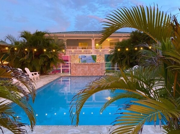 A swimming pool with a view of a building, surrounded by palm trees and string lights.