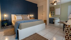 A bedroom with a bed, bedside tables, a nightstand, a mirror, and a ceiling fan.