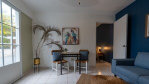 A living room with a blue sofa, a dining table with chairs, a large plant, and a painting on the wall.
